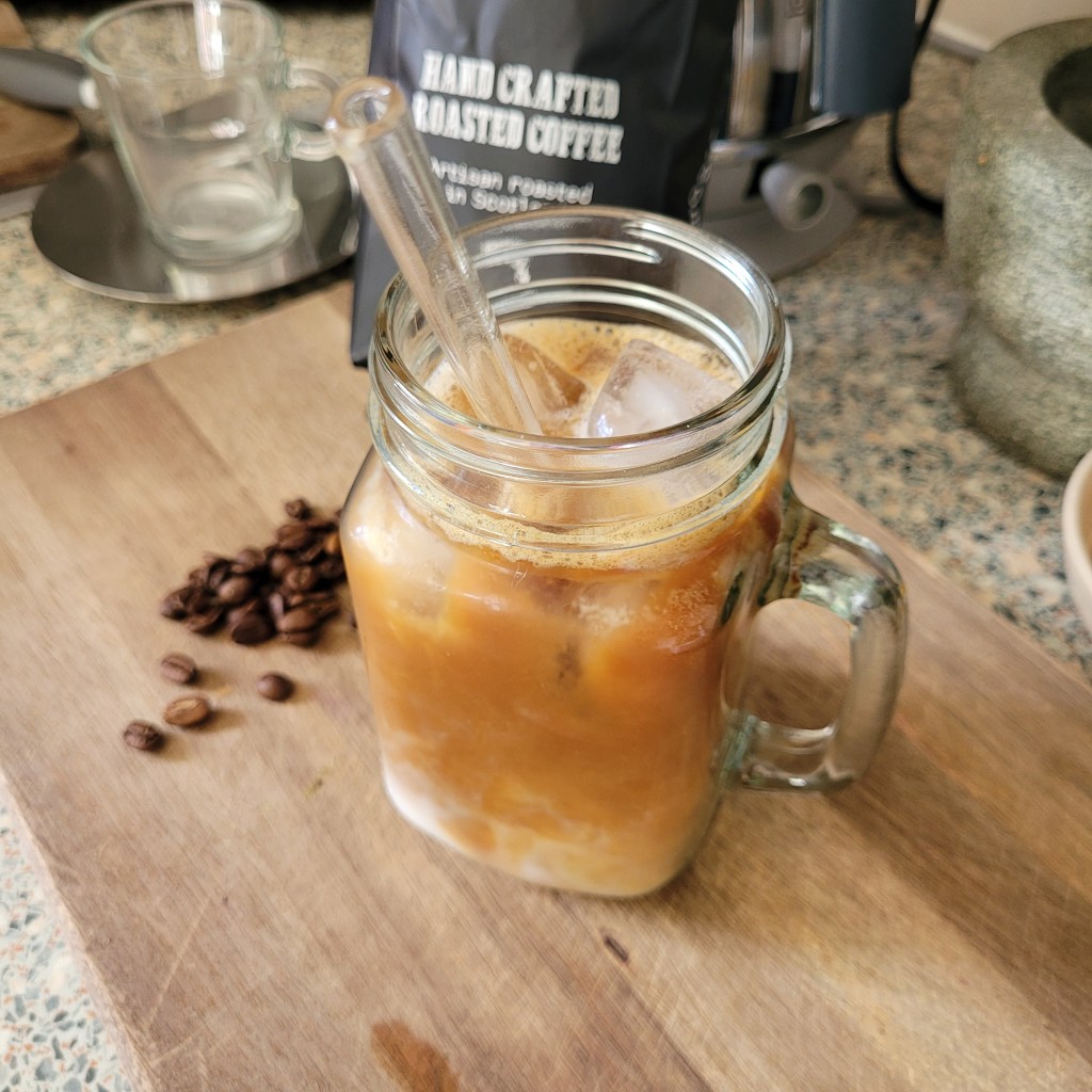 A glass cup with iced coffee and a straw.