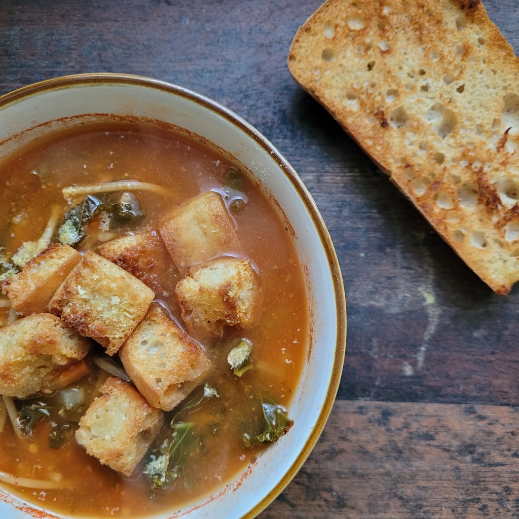 bowl of minestrone soup with croutons on top and a slice of crusty bread on the side