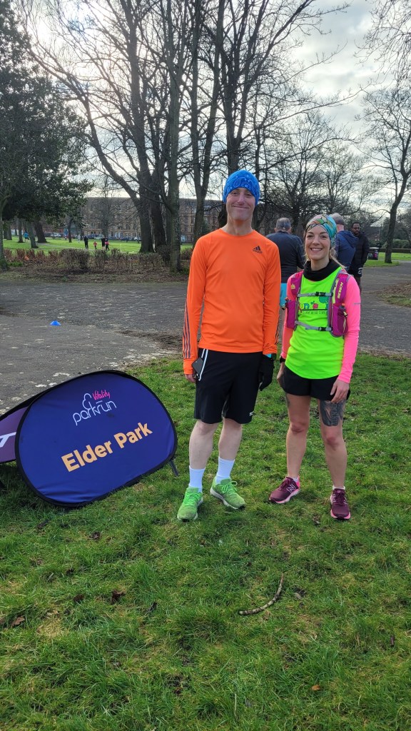 Kayleigh and a friend standing side by side at Park Run next to the sign "Elder Park"